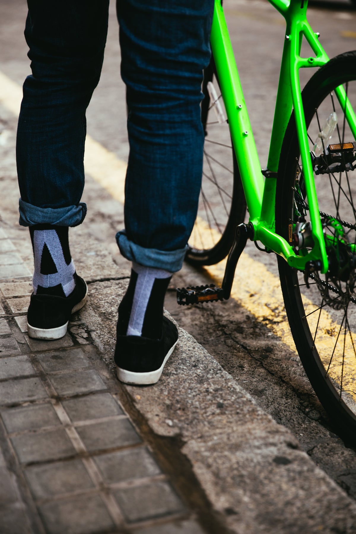 Picture of someone's legs and feet standing next to a green bicycle. 